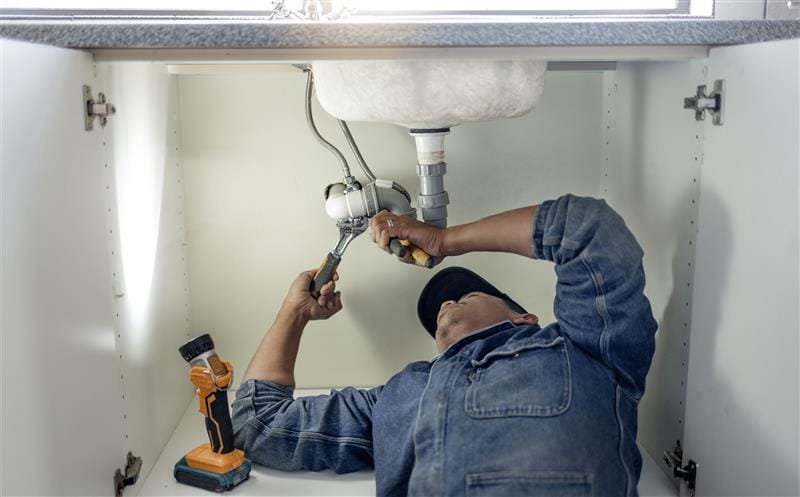 Plumber repairing pipes beneath a bathroom sink in Coral Gables