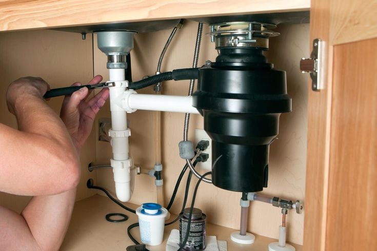 Plumber installing a garbage disposal beneath a kitchen sink in Coral Gables