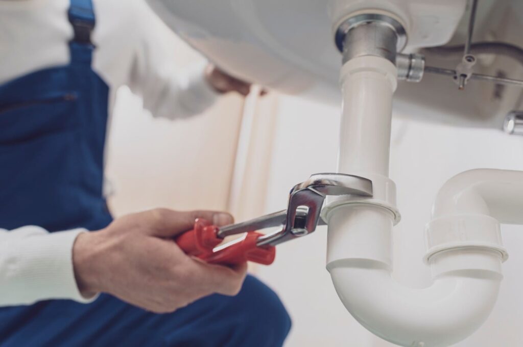 Plumber repairing a white drain pipe beneath a sink in Coral Gables