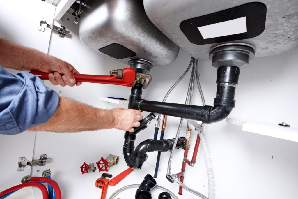 Plumber repairing drain pipes beneath a kitchen sink in Coral Gables